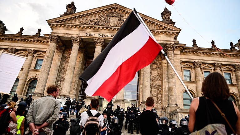 Teilnehmer einer Kundgebung gegen die Corona-Maßnahmen stehen vor dem Reichstag, ein Teilnehmer hält eine Reichsflagge. (Foto: dpa Bildfunk, picture alliance/dpa | Fabian Sommer)