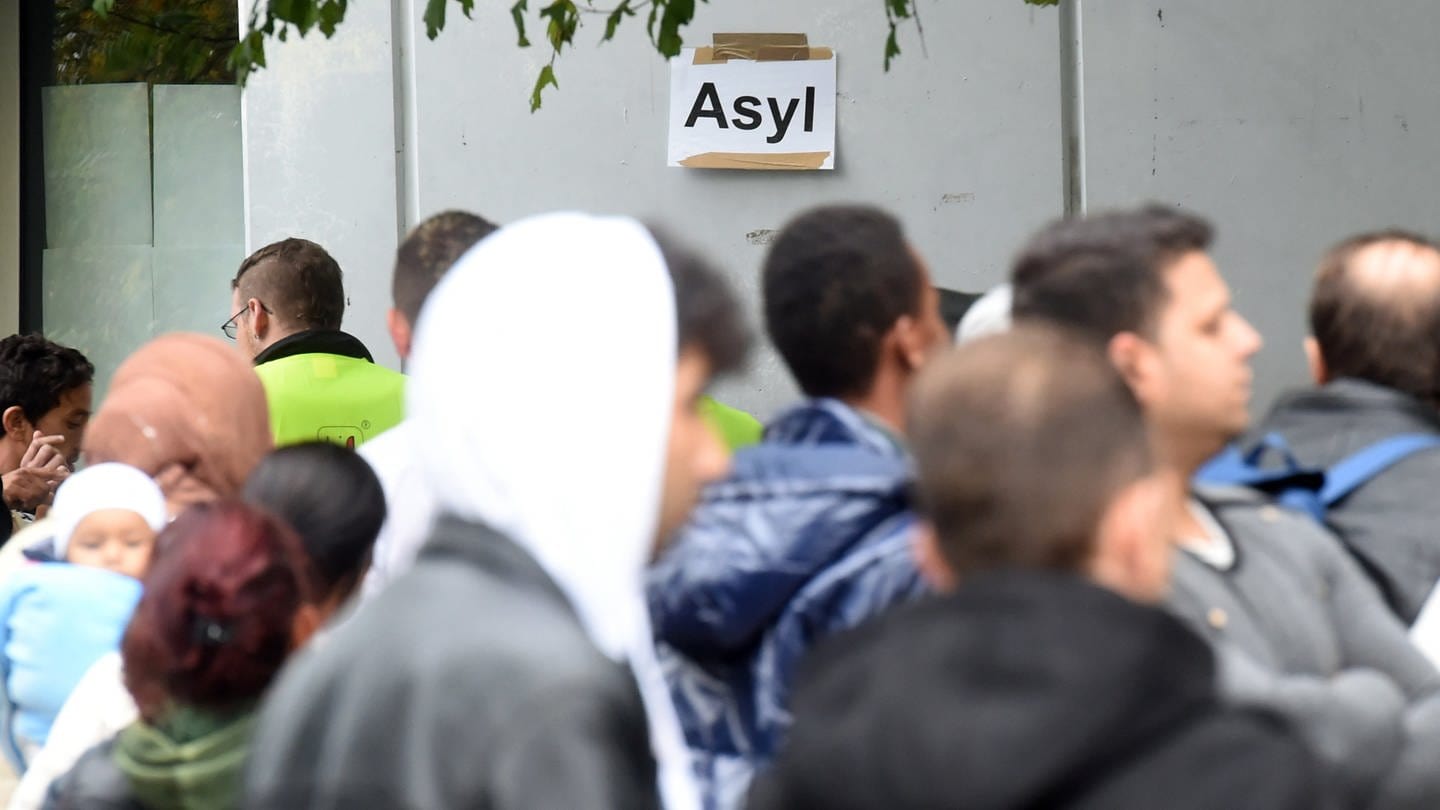 In der Landeserstaufnahmestelle (LEA) für Flüchtlinge in Karlsruhe (Baden-Württemberg) warten am 08.10.2014 Flüchtlinge auf ihre Registrierung. Im Hintergrund ist ein Papier an der Wand angebracht, auf dem das Wort 