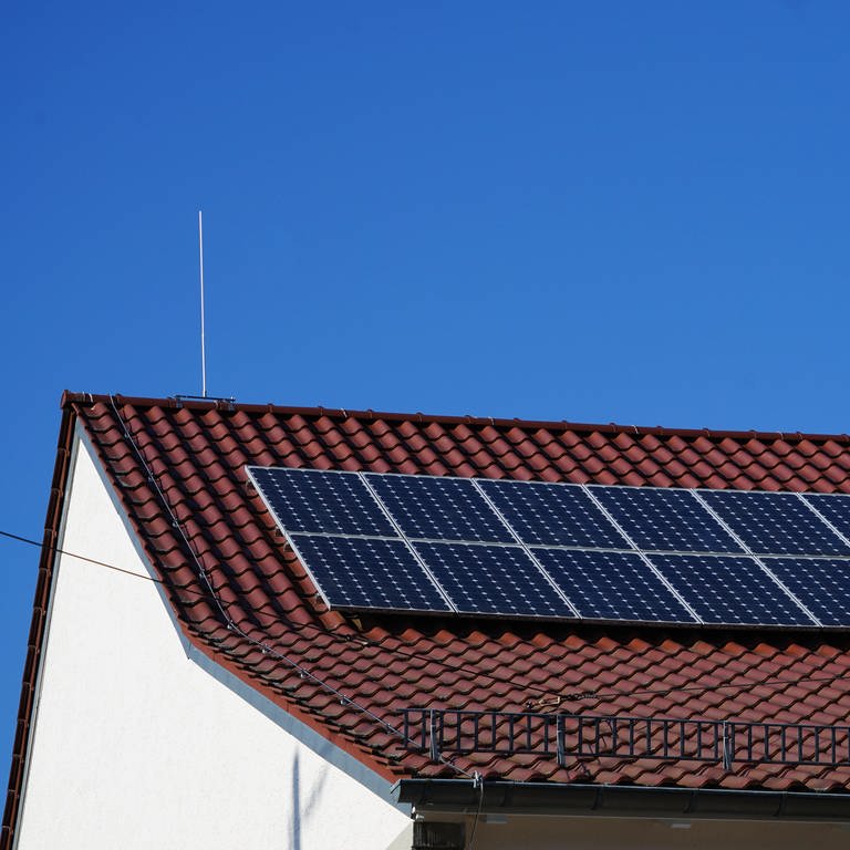 Solar Module auf einem Dach im Sonnenschein. Bei dem blauen Himmel kann im Frühling viel Strom produziert werden. Das Dach wird links und rechts von hohen Blitzableitern geschützt. (Foto: dpa Bildfunk, picture alliance / Zoonar | Yven Dienst)