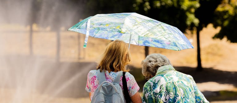 Zwei Frauen schützen sich am Rheinufer in der Kölner Altstadt mit einem Regenschirm vor der Sonne. (Foto: dpa Bildfunk, picture alliance/dpa | Rolf Vennenbernd)