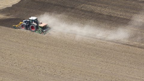 Ein Landwirt bearbeitet mit seinem Traktor ein ausgetrocknetes Feld und zieht eine Staubwolke hinter sich her. (Foto: dpa Bildfunk, picture alliance/dpa | Thomas Warnack)