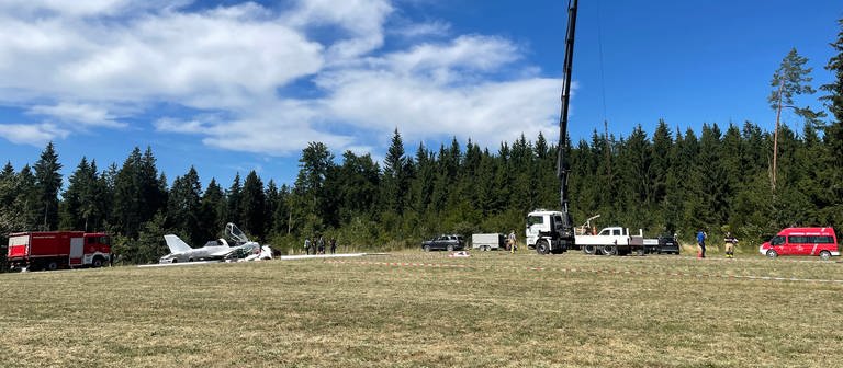 Auf einem Feld am Waldrand bei Böttingen (Kreis Tuttlingen) sind die Feuerwehr und ein Kran bei der Bergung eines abgestürzten Kleinflugzeugs.  (Foto: SWR)