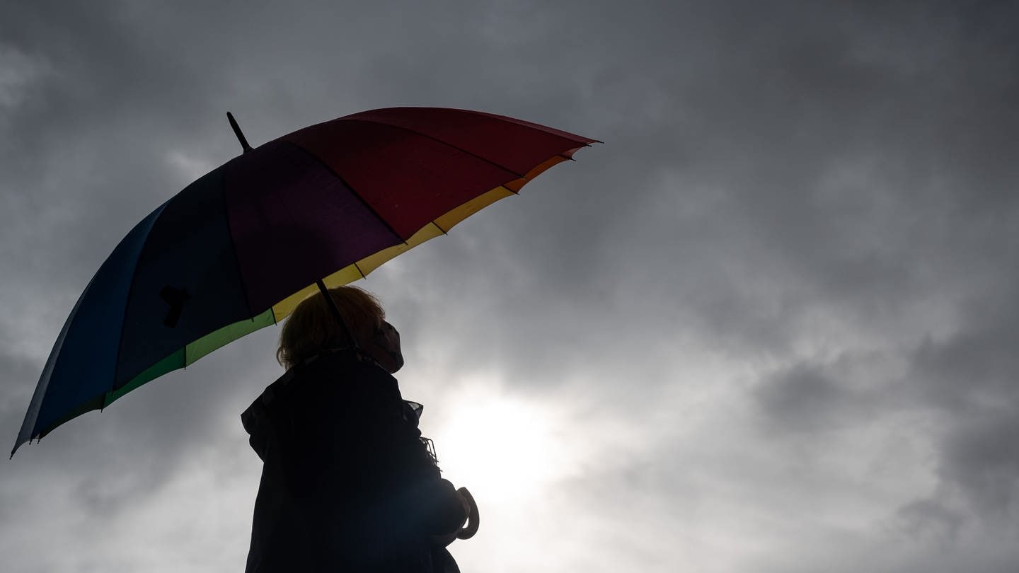 Frau hält Regenschirm und blickt zu Gewitterwolken.