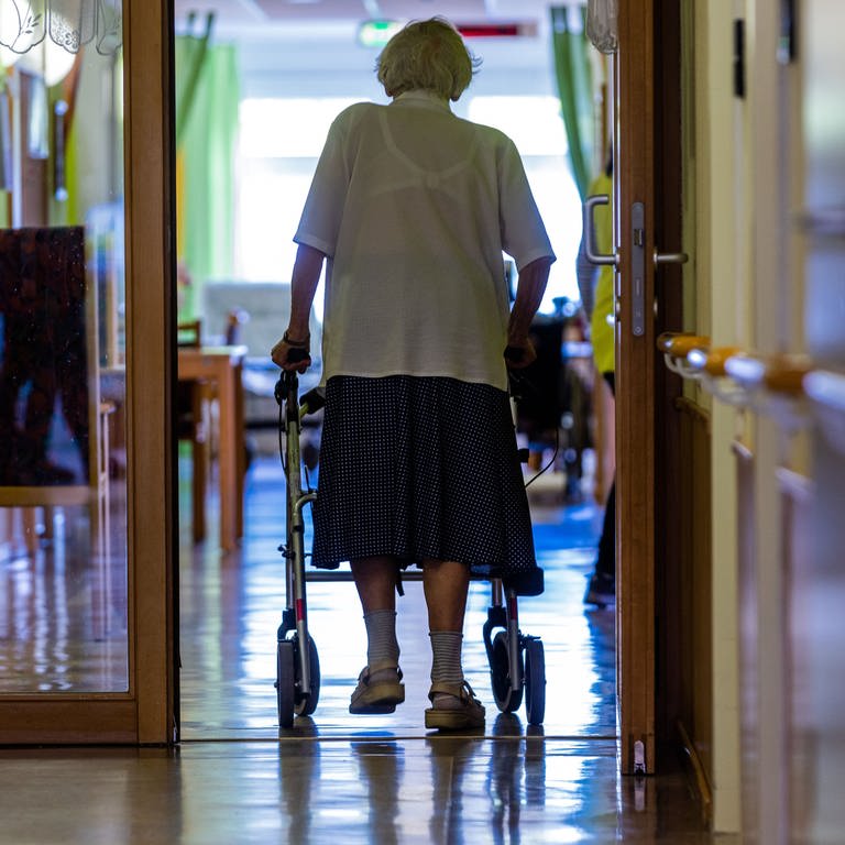 Eine Pflegeheimbewohnerin läuft mit Rollator über den Flur ihrer Einrichtung, die immer teurer wird. (Foto: dpa Bildfunk, picture alliance/dpa | Jens Büttner)
