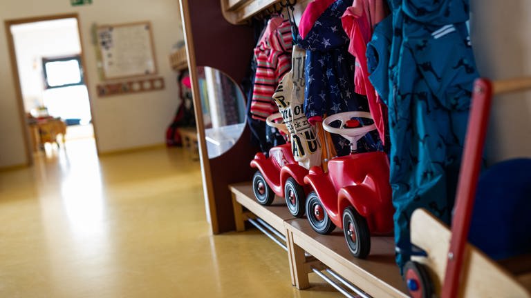 Bobbycars stehen unter Jacken von Kindern, die an einer Garderobe einer Kindertagesstätte (Kita) hängen.  (Foto: dpa Bildfunk, Philipp von Ditfurth)