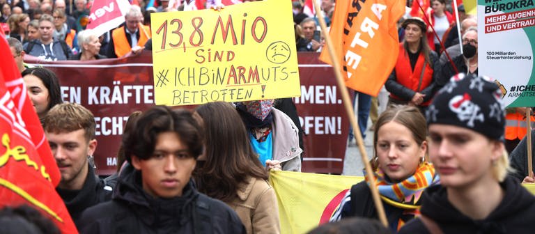 Eine Frau hält ein Schild mit der Aufschrift "13,8 Millionen sind arm, ich bin armutsbetroffen !" auf einer Demonstration unter dem Motto "Solidarisch aus der Krise – bezahlbares Leben für alle statt Profite für wenige." 29.10.2022 (Foto: dpa Bildfunk, picture alliance/dpa | Markus Scholz)