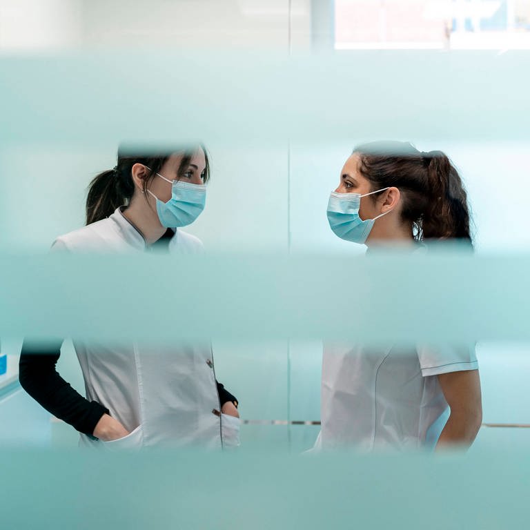 Zwei Arzthelferinnen stehen in einer Praxis und tragen einen Corona-Maskenschutz (Foto: IMAGO, IMAGO / Westend61)
