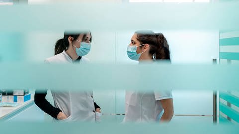 Zwei Arzthelferinnen stehen in einer Praxis und tragen einen Corona-Maskenschutz (Foto: IMAGO, IMAGO / Westend61)