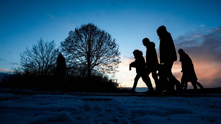 Spaziergänger gehen zur blauen Stunde über einen Feldweg. In vielen Teilen von Baden-Württemberg gab es den ersten Schnee, in höheren Lagen blieb dieser auch liegen. (Foto: dpa Bildfunk, picture alliance/dpa | Christoph Schmidt)