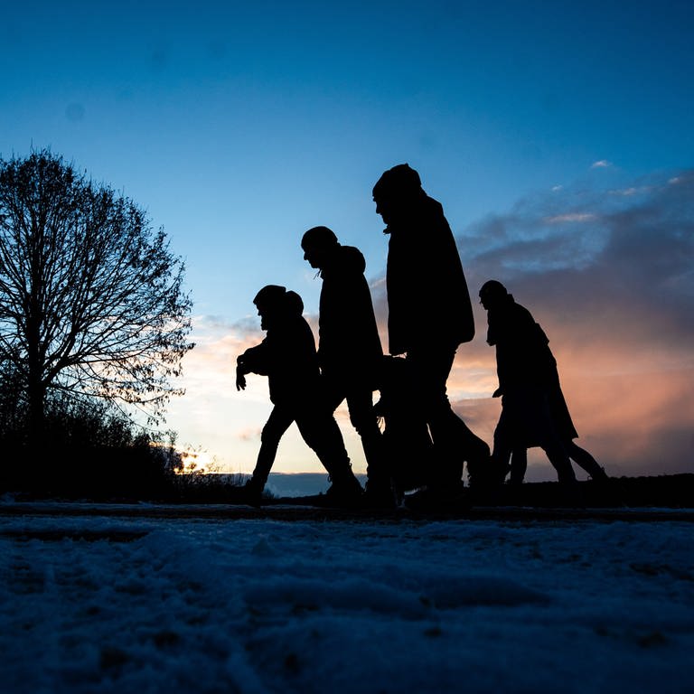 Spaziergänger gehen zur blauen Stunde über einen Feldweg. In vielen Teilen von Baden-Württemberg gab es den ersten Schnee, in höheren Lagen blieb dieser auch liegen. (Foto: dpa Bildfunk, picture alliance/dpa | Christoph Schmidt)