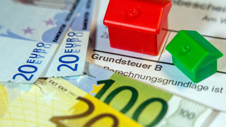 Ein Spielzeughaus und die Nachbildung von Euro-Geldscheinen liegen auf einem Abgabenbescheid für die Entrichtung der Grundsteuer. (Foto: dpa Bildfunk, picture alliance/dpa/dpa-Zentralbild | Jens Büttner)