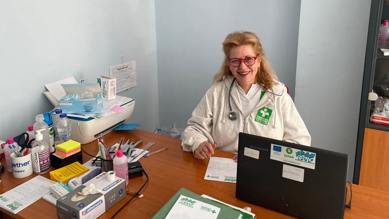 Irina von Zuboff sitzt im Arztkittel und mit Stethoskop um den Hals an einem Schreibtisch, (Foto: Irina von Zuboff )