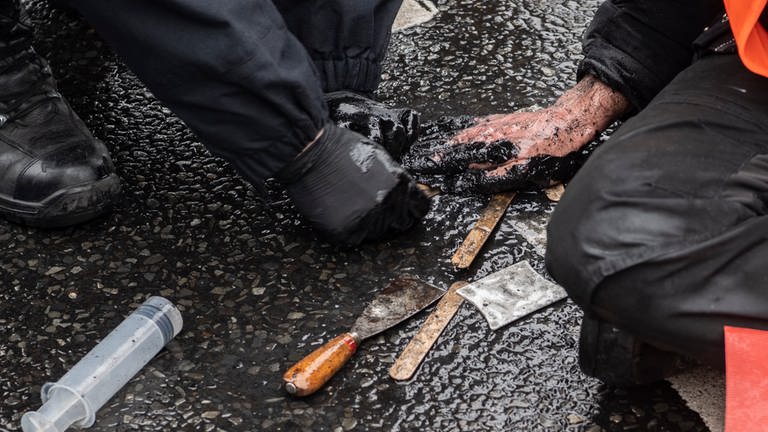 Ein Polizeibeamter versucht die festgeklebte Hand eines Demonstranten der Umweltschutzgruppe "Letzte Generation" vom Asphalt zu lösen.  (Foto: dpa Bildfunk, picture alliance/dpa | Paul Zinken (Symbolbild))