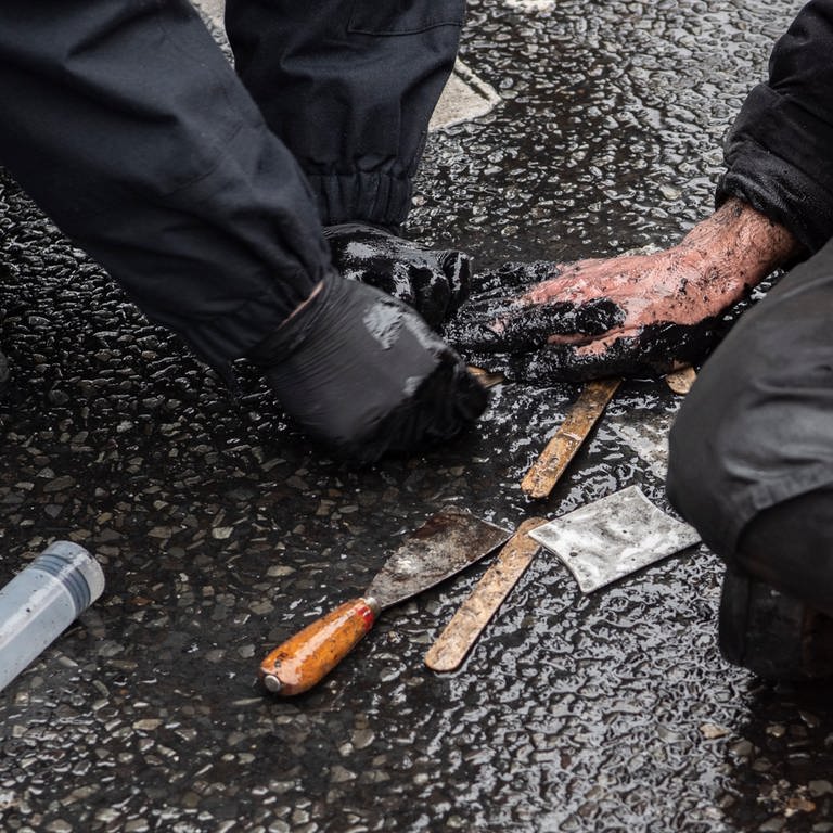 Ein Polizeibeamter versucht die festgeklebte Hand eines Demonstranten der Umweltschutzgruppe "Letzte Generation" vom Asphalt zu lösen.  (Foto: dpa Bildfunk, picture alliance/dpa | Paul Zinken (Symbolbild))