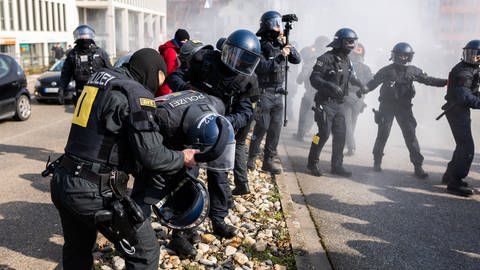 Ein von einem Pulverlöscher getroffener Polizist wird während einer Demonstration gegen den Landesparteitag der AfD Baden-Württemberg von zwei weiteren Polizisten versorgt. (Foto: dpa Bildfunk, picture alliance/dpa | Philipp von Ditfurth)