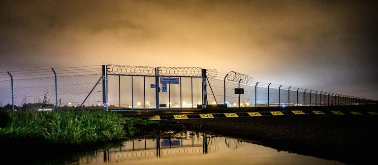 Der Zaun vor dem Rollfeld eines Flughafens im Morgengrauen.  (Foto: dpa Bildfunk, picture alliance/dpa | Mohssen Assanimoghaddam (Archivbild))