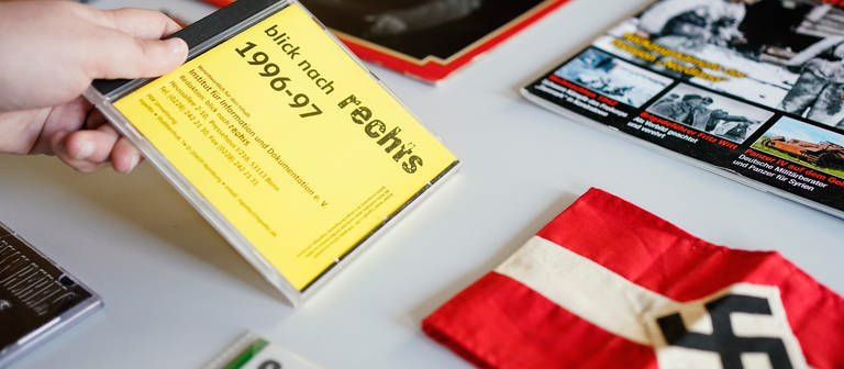 Eine Mitarbeiterin legt  in der Dokumentationsstelle Rechtsextremismus im Landesarchiv Baden-Württemberg eine CD mit der Aufschrift „blick nach rechts 1996-97“ auf einen Tisch mit Ausstellungsobjekten. (Foto: dpa Bildfunk, picture alliance/dpa | Uwe Anspach)