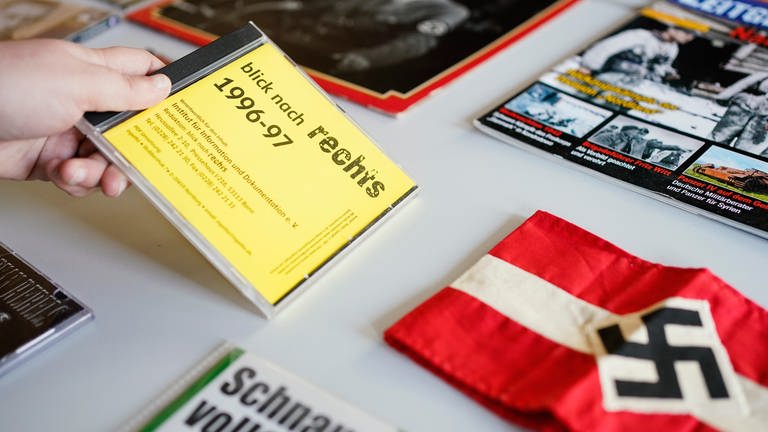 Eine Mitarbeiterin legt  in der Dokumentationsstelle Rechtsextremismus im Landesarchiv Baden-Württemberg eine CD mit der Aufschrift „blick nach rechts 1996-97“ auf einen Tisch mit Ausstellungsobjekten. (Foto: dpa Bildfunk, picture alliance/dpa | Uwe Anspach)