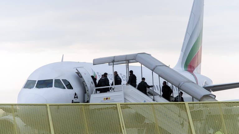 Flugzeug mit einsteigenden Passagieren, dabei erkennbar Polizei an den Türen, im Vordergrund ein gelber Zaun. (Foto: dpa Bildfunk, picture alliance / dpa | Daniel Maurer)