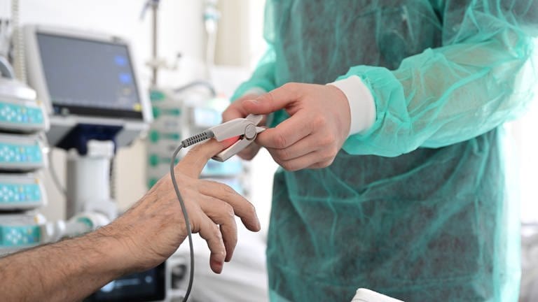 Ein Pfleger legt in einem Krankenzimmer im Klinikum Stuttgart bei einem Patienten ein Messgerät an. (Foto: dpa Bildfunk, picture alliance/dpa | Bernd Weißbrod)