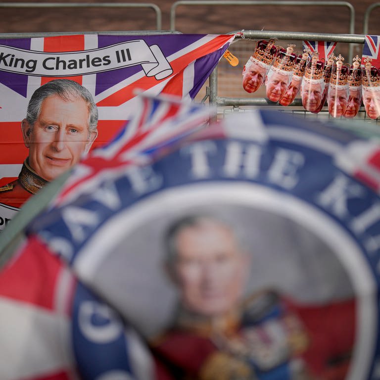 Gesicht von König Charles auf Fanartikeln, dazu die britische Flagge (Foto: dpa Bildfunk, picture alliance/dpa/AP | Andreea Alexandru)