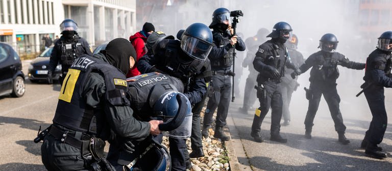 Ein von einem Pulverlöscher getroffener Polizist wird während einer Demonstration gegen den Landesparteitag der AfD Baden-Württemberg von zwei weiteren Polizisten versorgt. (Foto: dpa Bildfunk, picture alliance/dpa | Philipp von Ditfurth)