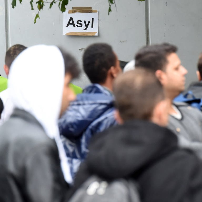  In der Landeserstaufnahmestelle (LEA) für Flüchtlinge in Karlsruhe (Baden-Württemberg) warten am 08.10.2014 Flüchtlinge auf ihre Registrierung. Im Hintergrund ist ein Papier an der Wand angebracht, auf dem das Wort "Asyl" steht. 