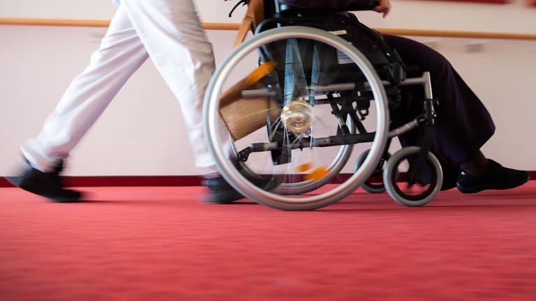 Ein Pfleger eines Pflegeheims schiebt eine Bewohnerin mit einem Rollstuhl. (Foto: dpa Bildfunk, picture alliance/dpa | Tom Weller)