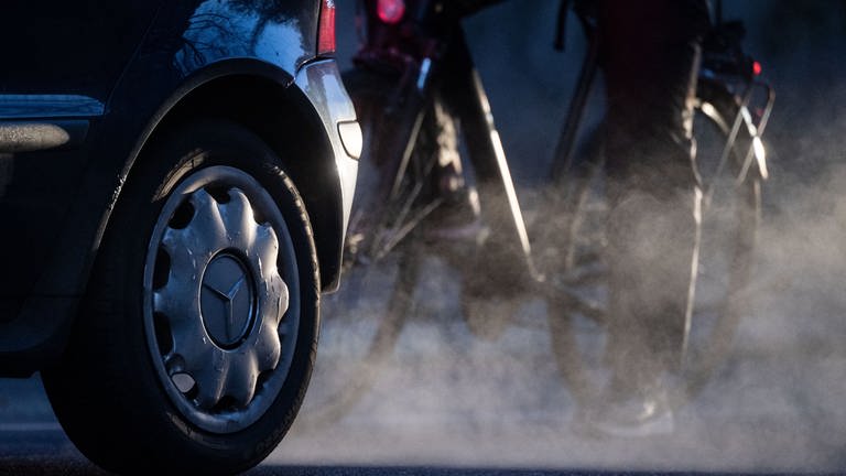Ein Radfahrer steht neben einem Auto von Mercedes mit Dieselantrieb, dessen Abgase in der kalten Morgenluft sichtbar werden (Symbolbild).  (Foto: dpa Bildfunk, picture alliance/dpa | Marijan Murat)