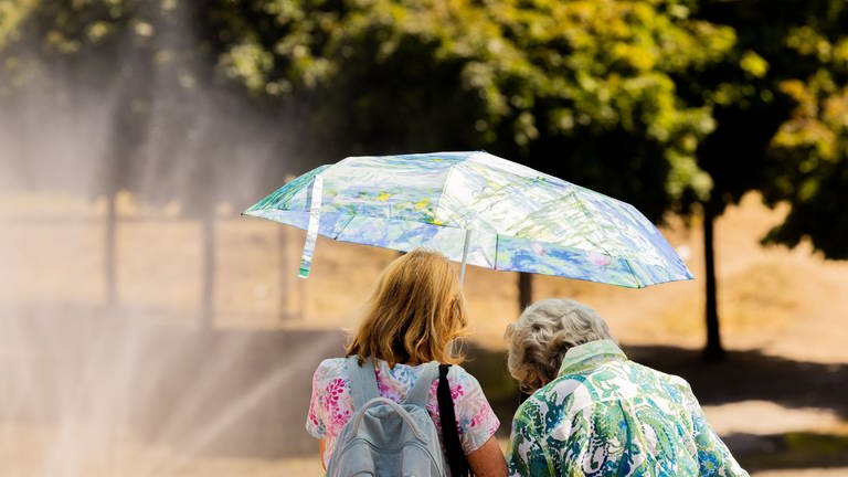 Zwei Frauen schützen sich am Rheinufer in der Kölner Altstadt mit einem Regenschirm vor der Sonne. (Foto: dpa Bildfunk, picture alliance/dpa | Rolf Vennenbernd)