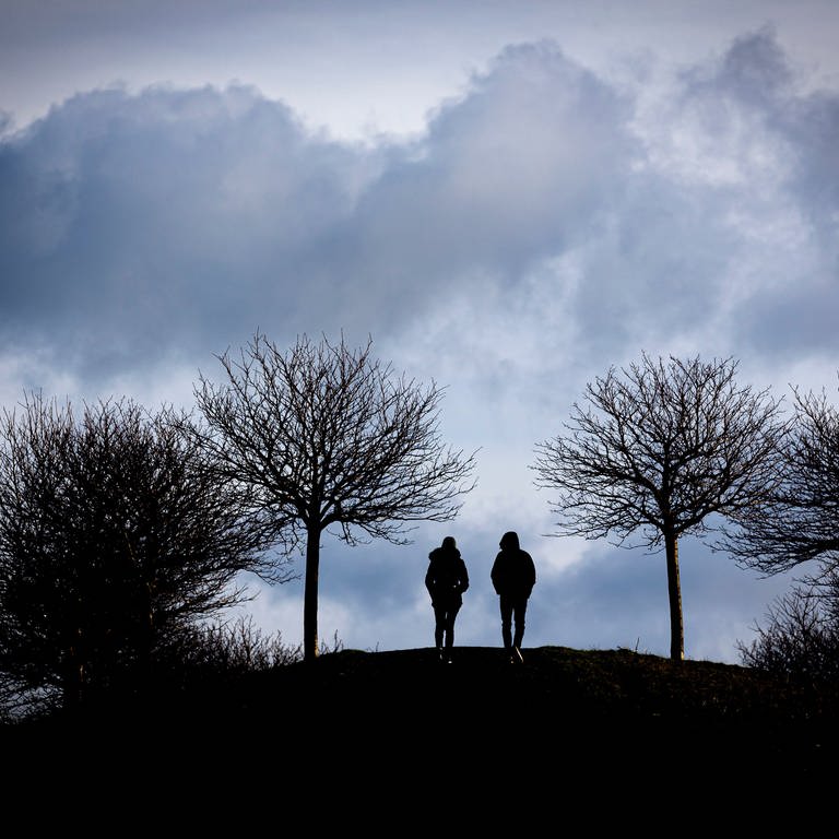 Spaziergänger gehen auf einen Hügel am Kronsberg, während bei stürmischem Wetter dunkle Wolken am Horizont vorüberziehen. (Foto: dpa Bildfunk, picture alliance/dpa | Moritz Frankenberg (Symbolfoto))