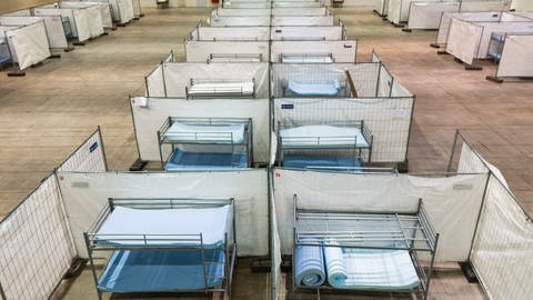 Stockbetten stehen zwischen Zäunen in einer Notunterkunft für Asylsuchende: Städte und Gemeinden in BW suchen händeringend nach Unterkünften für Geflüchtete (Symbolbild). (Foto: dpa Bildfunk, picture alliance/dpa | Philipp von Ditfurth)