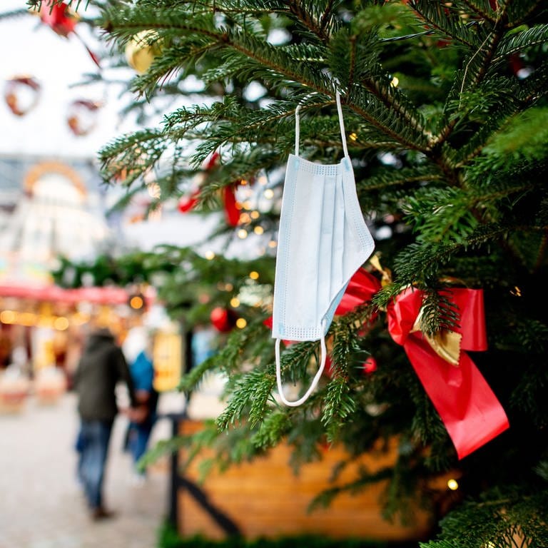 Eine Corona-Maske hängt an einem verzierten Weihnachtsbaum (Foto: dpa Bildfunk, Picture Alliance)