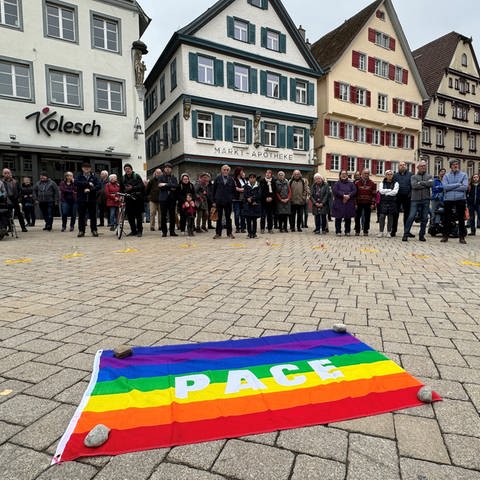 Mehrere Menschen haben sich in einem Halbkreis aufgestellt und die Friedensflagge in die Mitte gelegt.  (Foto: SWR)