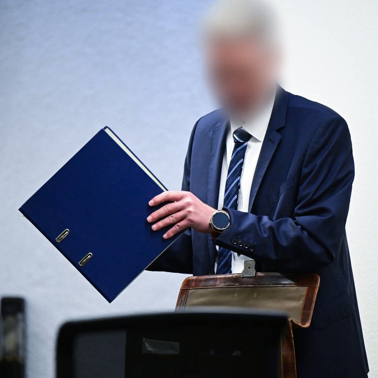 Archivbild: Der Angeklagte, inzwischen suspendierte Inspekteur der Polizei in Baden-Württemberg, nimmt zu Beginn seines Prozesses im Gerichtssaal einen Ordner aus seiner Tasche.