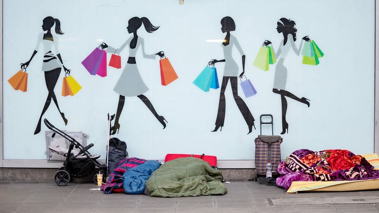 Menschen schlafen vor einem Schaufenster mit Aufklebern, die Personen mit Einkaufstüten zeigen. (Foto: dpa Bildfunk, picture alliance/dpa | Marijan Murat (Symbolfoto))