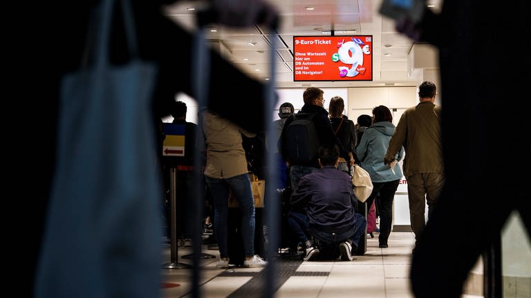 Kunden stehen in einer Schlange unter einem Hinweißschild für das 9-Euro-Ticket im Reisezentrum der Deutschen Bahn im Berliner Hauptbahnhof. (Foto: dpa Bildfunk, picture alliance/dpa | Carsten Koall)