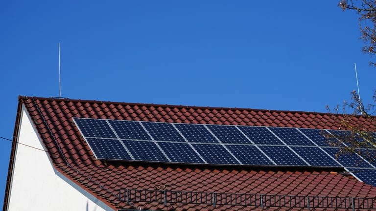 Solar Module auf einem Dach im Sonnenschein. Bei dem blauen Himmel kann im Frühling viel Strom produziert werden. Das Dach wird links und rechts von hohen Blitzableitern geschützt. (Foto: dpa Bildfunk, picture alliance / Zoonar | Yven Dienst)