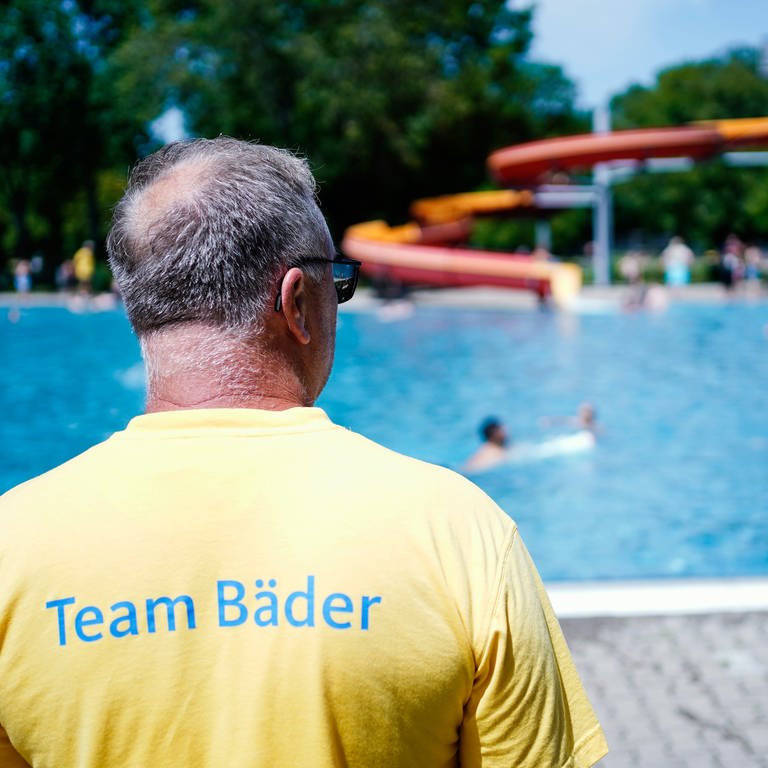 Ein Schwimmmeister steht im Herzogenriedbad in Mannheim vor einem Schwimmbecken mit Wasserrutsche. (Foto: dpa Bildfunk, picture alliance/dpa | Uwe Anspach)
