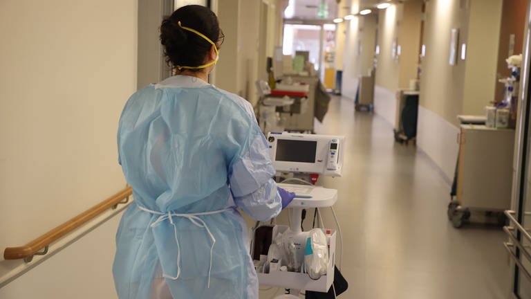 Eine Krankenschwester läuft mit medizinischem Gerät auf der Corona-Normalstation den Gang entlang.