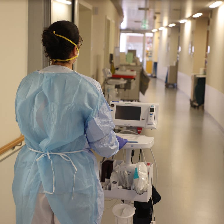 Eine Krankenschwester läuft mit medizinischem Gerät auf der Corona-Normalstation den Gang entlang.