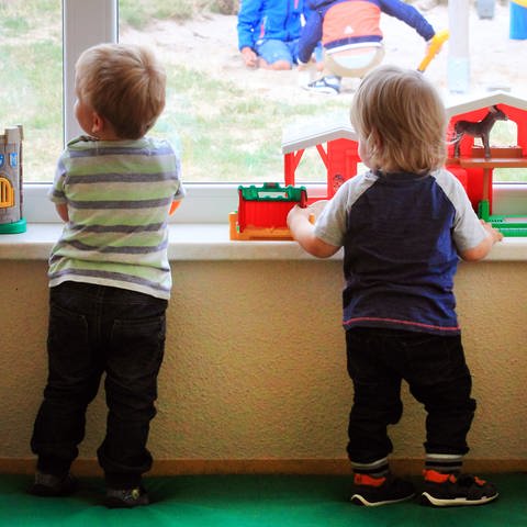 Zwei kleine Kinder spielen am Fenster in einer Kindertagesstätte.