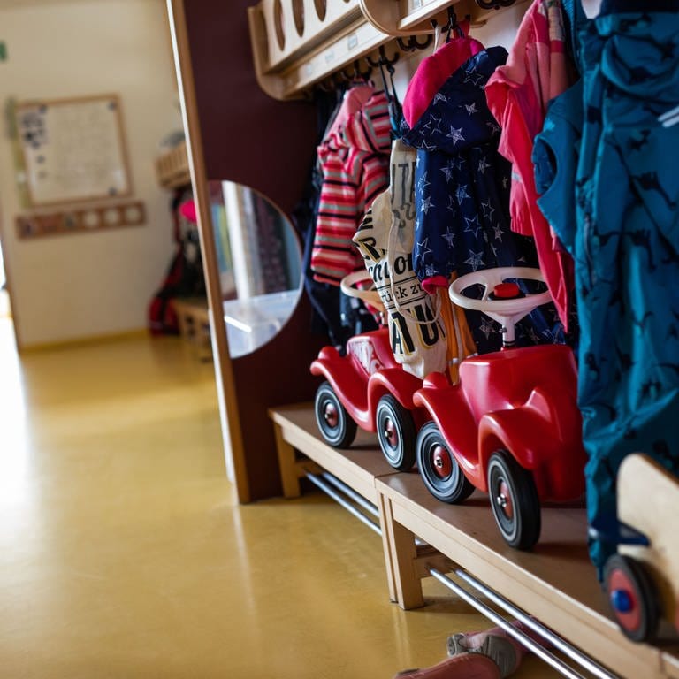 Bobbycars stehen unter Jacken von Kindern, die an einer Garderobe einer Kindertagesstätte (Kita) hängen.  (Foto: dpa Bildfunk, Philipp von Ditfurth)