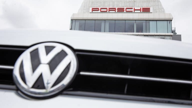 Das Volkswagen-Logo ist am Porsche-Firmensitz in Stuttgart-Zuffenhausen vor einem Gebäude mit einem Porsche Schriftzug zu sehen.  (Foto: dpa Bildfunk, picture alliance/dpa | Christoph Schmidt)