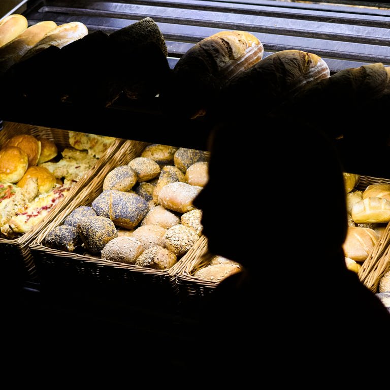 picture alliancedpa | Julian Stratenschulte (Foto: dpa Bildfunk, Eine Bäckereifachverkäuferin steht am frühen Morgen in der bewusst sparsam beleuchteten Bäckerei)