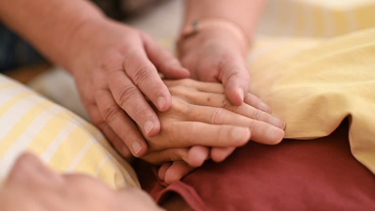 Symbolbild: Eine Hospizmitarbeiterin hält die Hand eines Menschen. (Foto: dpa Bildfunk, picture alliance/dpa | Felix Kästle (Symbolbild))