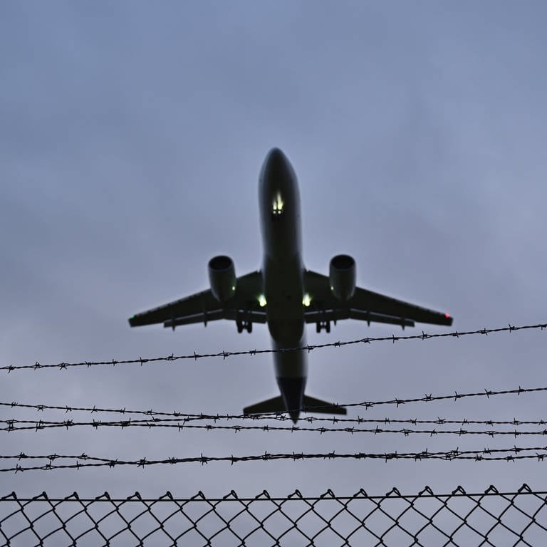 Ein Flugzeug fliegt über einen mit Stacheldraht gesicherten Maschendrahtzaun.  (Foto: dpa Bildfunk, Daniel Kubirski)