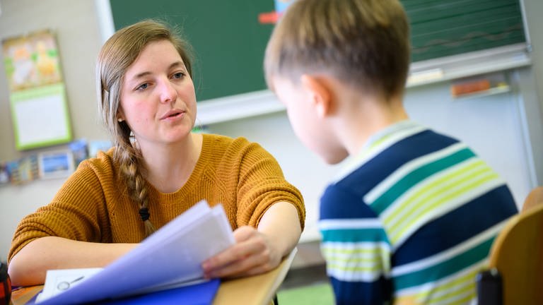 Eine Lehrerin erklärt in einer Grundschule einem Schüler seinen Wochenplan für die kommenden Wochen.