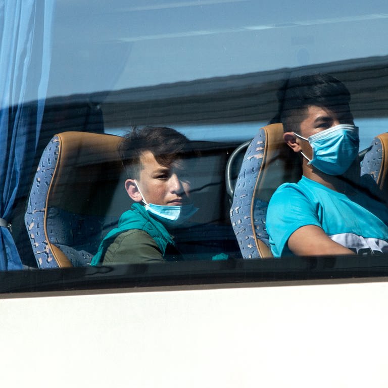 Junge Flüchtlinge, teilweise mit Mundschutz, sitzen in einem Bus (Foto: dpa Bildfunk, picture alliance/dpa | Hauke-Christian Dittrich)