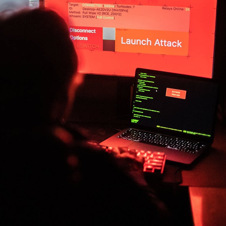 Ein Mann sitzt vor Bildschirmen, die Hacker-Programme und eine fiktive Fernlösch-Software zeigen. 